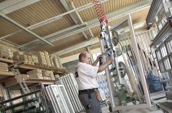 Ein fertig montiertes Fenster wird mittels Kran vom Arbeitstisch angehoben und zum Transportwagen gebracht