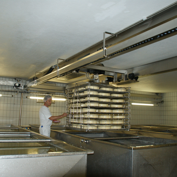 Eine Hurde mit Käselaiben wird, präzise positioniert, ins Salzbad abgesenkt